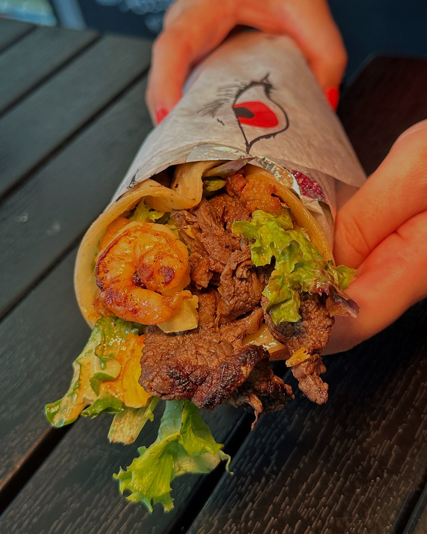 Close-up of a gourmet wrap with grilled steak, shrimp, fresh lettuce, and signature sauce from Wolfnights